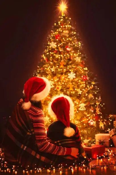 Photo of Christmas Family Looking Lighting Xmas Tree, Mother and Child in Red Santa Hats, New Year Night