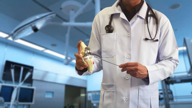 orthopedic doctor showing model of total knee replacement(tkr) with blurred background of operative bed in modern operating room. medical technology and operative care concept. - osteoarthritis doctor medicine healthcare and medicine imagens e fotografias de stock