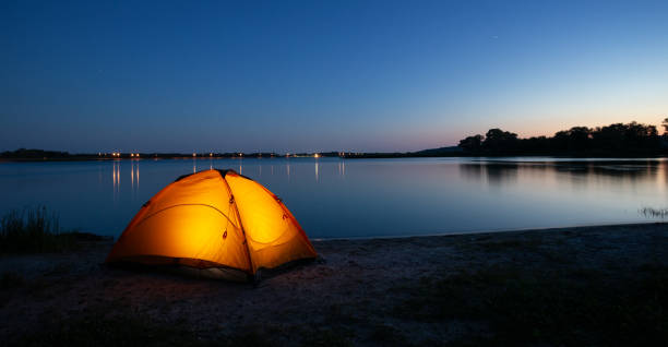 istock Orange interior lit tent on a lake at dusk 1182010083