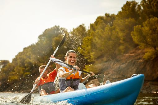 Heterosexual couple enjoying kayaking on river. Cheerful man and woman are paddling kayak together. They are on summer vacation.