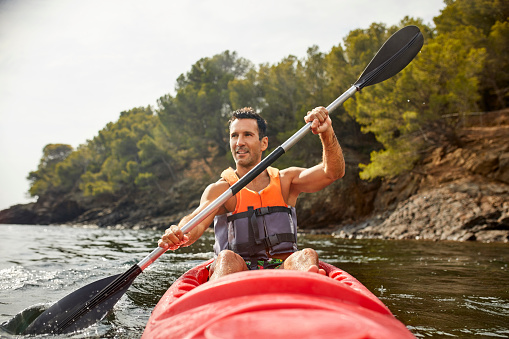Smiling mature man looking away while paddling kayak. Male is enjoying aquatic sport during summer. He is on vacation.