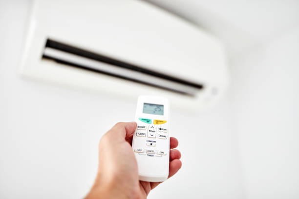 istock Modern air conditioner unit with a hand holding a remote. 1182012580