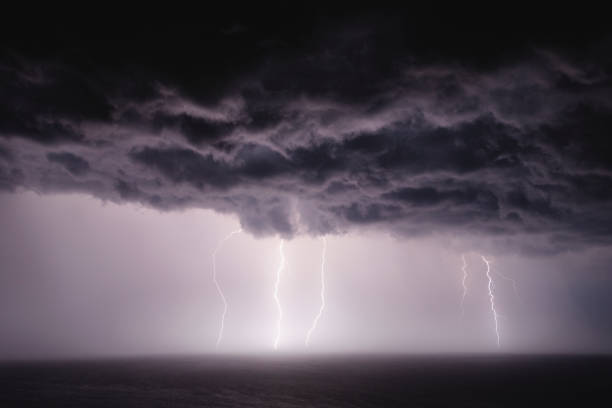 Dark storm clouds with rain and lightning over sea at night.