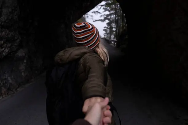 Photo of Follow me, Woman holding hand and walking through stone tunnel in the rocky mountain forest