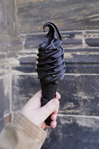 black soft serve ice cream - hand holding cone wih activated charcoal icecream