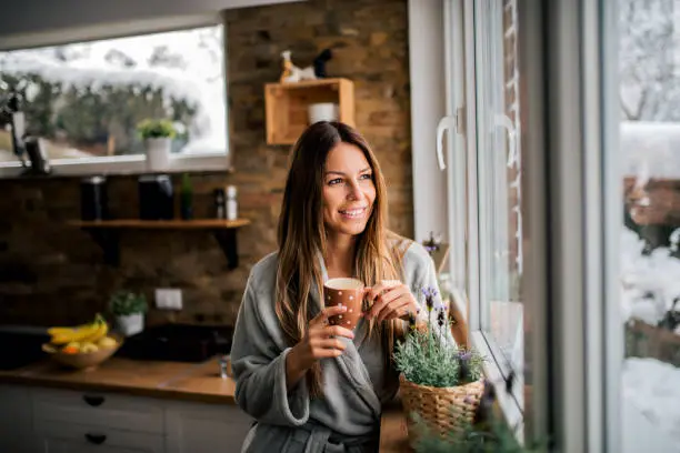 Photo of Young woman drinking coffee in the morning, looking at window.