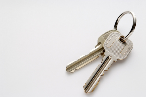 Keys with keychain in shape of house on grey wooden table, closeup. Space for text