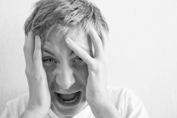 istock 18 year old guy squeezes his head with his hands and screams 1182044976