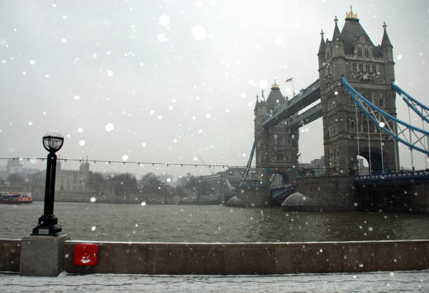 istock Snow fall around London's Tower Bridge, River Thames, footpath and Victorian lantern with an overcast grey sky 1182051707