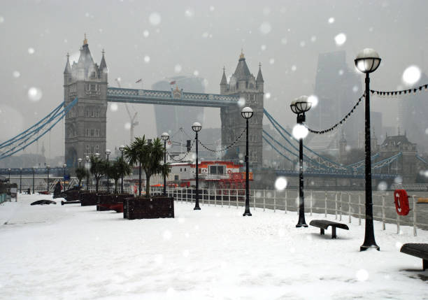 Snow fall around Tower Bridge, River Thames, footpath and Victorian lanterns with an overcast grey sky and city skyline in the background Famous London tourist attraction and skyscrapers in the cold, winter Christmas weather winter wonderland london stock pictures, royalty-free photos & images