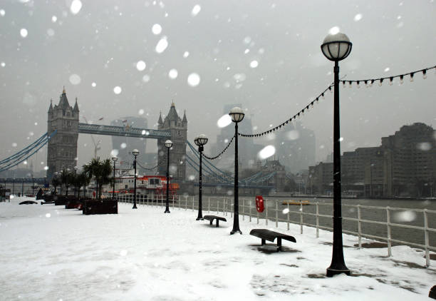 istock Snow fall around Tower Bridge, River Thames, footpath and Victorian lanterns with an overcast grey sky and city skyline in the background 1182053570