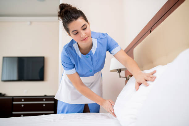 istock Pretty young professional chamber maid putting white clean pillows on bed 1182054585