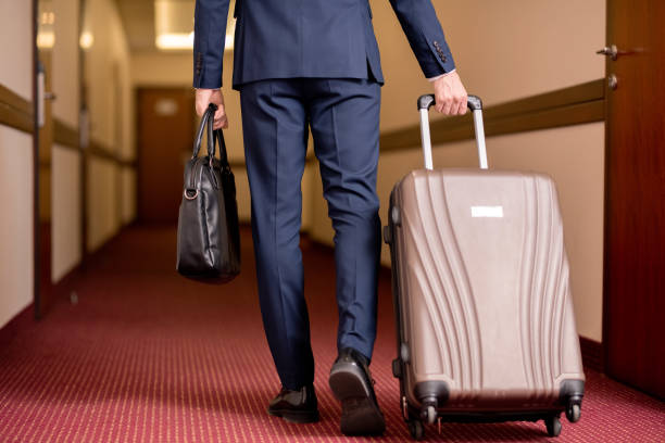 istock Young businessman in suit carrying black leather handbag and pulling suitcase 1182054669