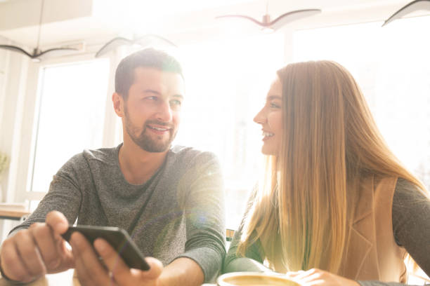 istock Happy young affectionate couple with smartphone discussing funny stuff in cafe 1182060578