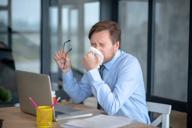 istock Man sitting in front of laptop and sneezing while having flu 1182061495