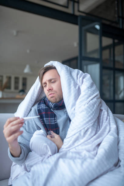 istock Man covered in bedsheet feeling sad after measuring temperature 1182062869