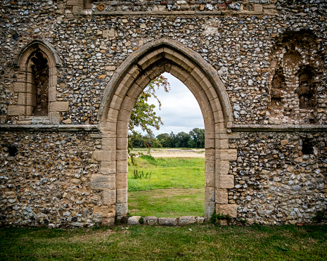 View through a Gothic arch in the ruins of the medieval Carmelite Friary of St Mary at Burnham Norton in North Norfolk, Eastern England, on a sunny September day. The friary was constructed in 1253 and fell into disuse before the Reformation.