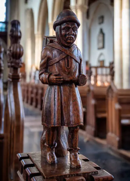 Photo of Victorian carving of the Pedlar of Swaffham on a pew end in St Peter & St Paul Church