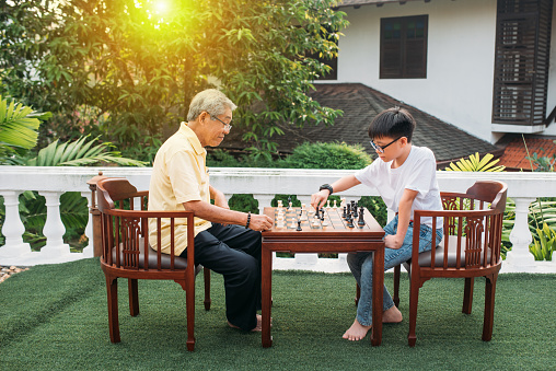 Image of Asian grandfather teaching his grandson playing chess.