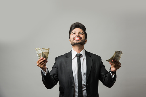Happy bearded Indian businessman holding fan in hand, Indian Rupee currency bills of 500 , standing isolated over white background