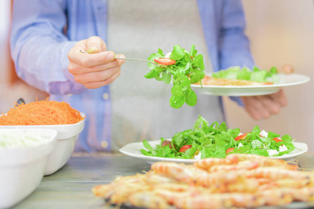 Man in blue shirt whose hands and abdomen are seen serving vegetables using a fork, with the background out of focus. Healthy food concept.
