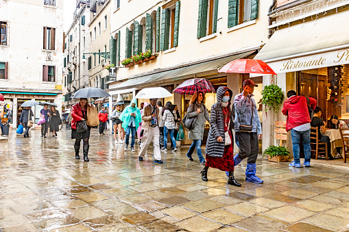 Rainy day on Campo Santi Filippo e Giacomo Venice. Tourists walking through the piazza near The Bridge of sighs with wet weather clothing and umbrellas.