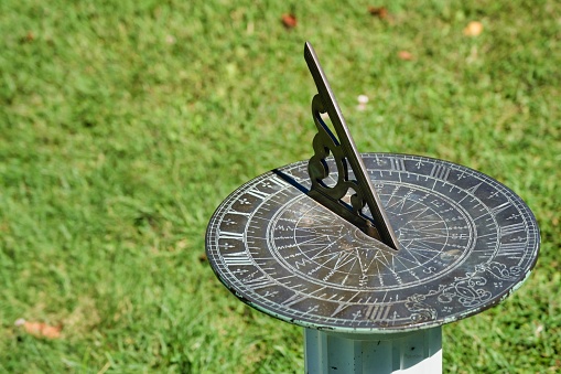 Vintage metal sundial in the sunlight, on a post in the grass