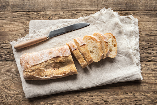 Ciabatta - Fresh Homemade Italian Bread sliced on napkin, wooden table, top view.