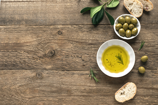 Olive Oil. Organic olive oil  in bowl with green olives, rosemary and ciabatta bread on wooden background ,top view, copy space. Healthy mediterranean food concept.
