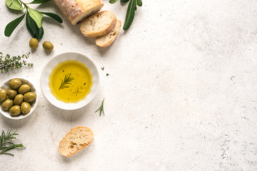 Olive Oil and Bread. Organic olive oil with green olives in bowl, herbs and ciabatta bread on white background with copy space, healthy mediterranean food concept.