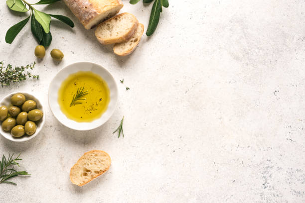 Olive Oil Olive Oil and Bread. Organic olive oil with green olives in bowl, herbs and ciabatta bread on white background with copy space, healthy mediterranean food concept. green olive fruit stock pictures, royalty-free photos & images