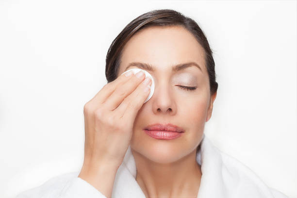 istock Beautiful woman removing her makeup using a cotton round wearing a white bathrobe over a white background 1182079924