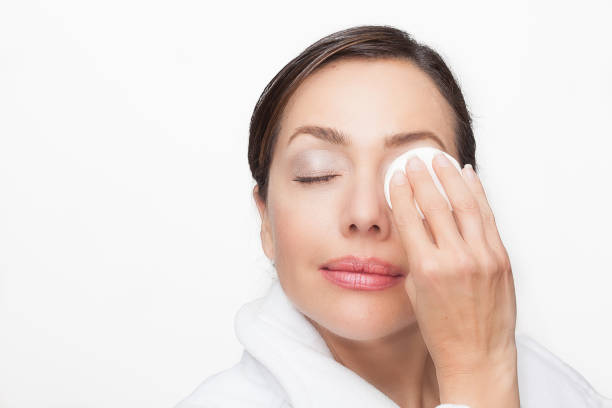 istock Beautiful woman removing her makeup using a cotton round wearing a white bathrobe over a white background 1182079930