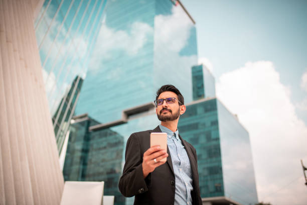 Businessman near skyscrapers Young businessman near skyscrapers using the smartphone directly below stock pictures, royalty-free photos & images