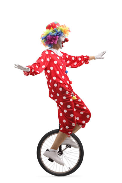 Cheerful clown riding a unicycle and making a funny grimace Full length profile shot of a cheerful clown riding a unicycle and making a funny grimace isolated on white background clown photos stock pictures, royalty-free photos & images