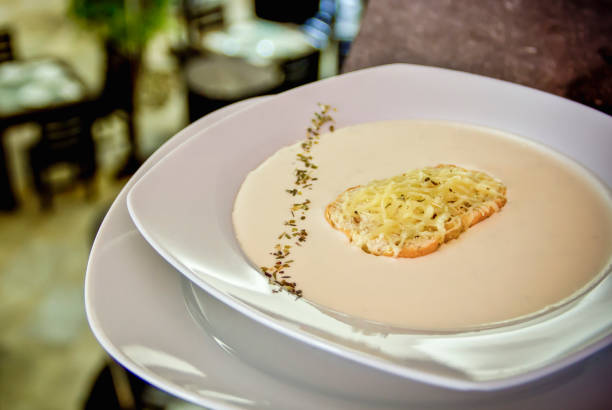 Close-up of a spoon lifting a flavorful portion of pumpkin soup topped with a crouton and microgreens. The focus on texture and garnish highlights the soup's rich and creamy consistency. This appetizing close-up is perfect for cookbooks, culinary blogs, and advertisements related to fine dining, autumn recipes, and seasonal cuisine.