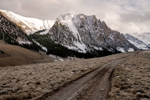 istock Dirt road leads along a mountain ridge with snow and clouds 1182087782