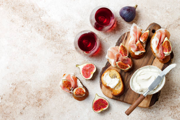 crostini mit schinken, frischkäse und feigen auf holzbrett. vorspeisen, antipasti-snacks und rotwein in gläsern. authentische traditionelle spanische tapas-set. hellbeige hintergrund. ansicht von oben - bread cheese bruschetta canape stock-fotos und bilder