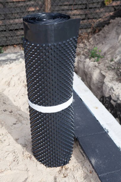 istock View of the house under construction, scaffolding, insulation from foamed polystyrene walls covered with black waterproof film, sand and mud instead of the floor. Effective waterproofing of the bucket foil of the foundation of the house being built 1182094894