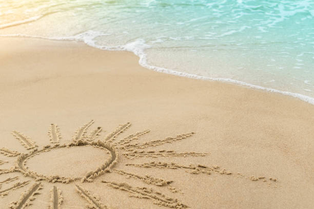 istock Sun drawn on seashore sand and wave with foam 1182095490