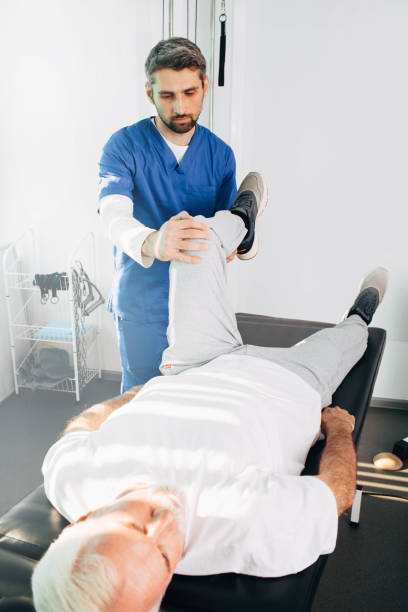istock physiotherapist treating leg injury on a man lying down. Senior man training with his therapist. Joint, knee and leg pain treatment 1182097319