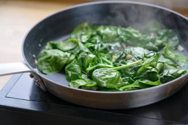 hojas de espinacas fritas en una sartén en la estufa, concepto de cocina saludable - espinaca fotografías e imágenes de stock