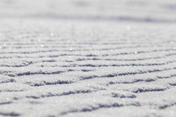 Snow surface, winter - snow drifts after the past snowfall. On the surface irregularities from strong winds were formed. Photo close-up at an angle with a shallow depth of field