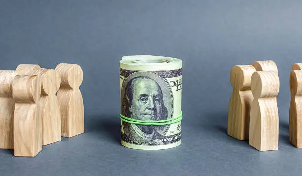 Photo of Two groups of people are divided by a bundle roll dollars. The cult of money, capitalism. Financial instruments and education. Decent salary wages. Investment concept. High profits and a welcome item.