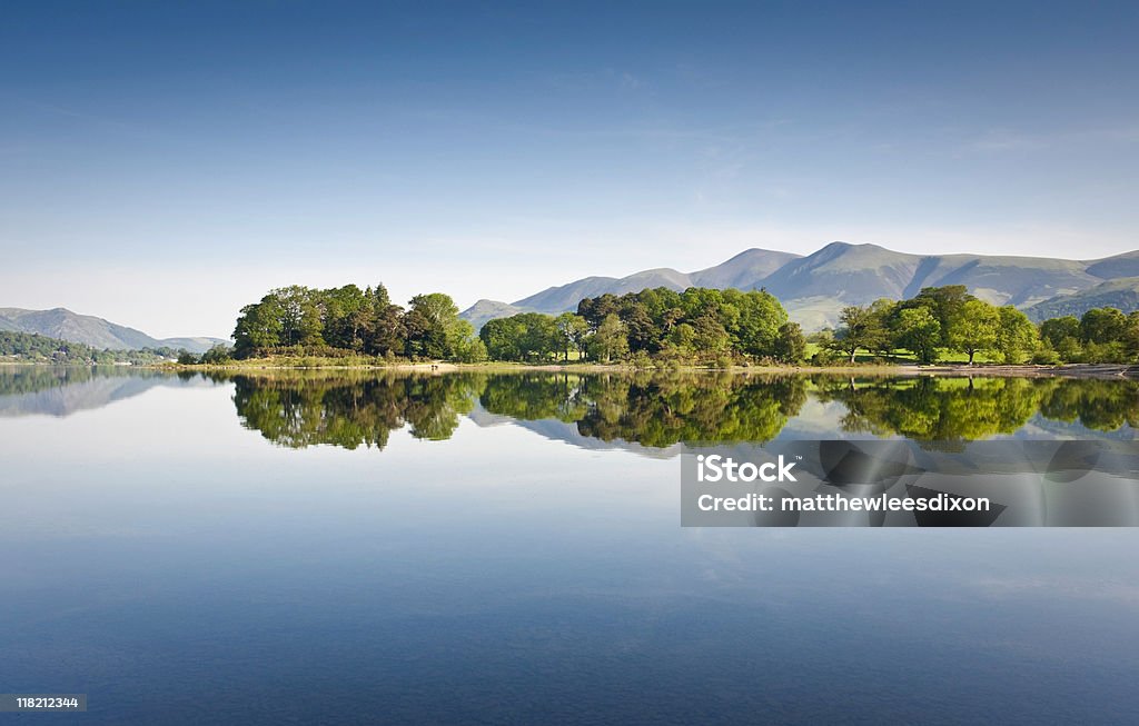 Scenic image of a lake with clear reflection of the scenery Summer woodland reflected in a perfectly still Derwent Water with dramatic Latrigg mountain backdrop in the beautiful English Lake District. ProPhoto profile for precise color reproduction. English Lake District Stock Photo