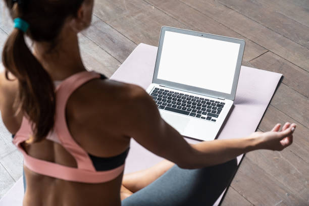 la parte trasera de atrás sobre la vista del hombro en el ajuste deportivo saludable calma mujer sentarse en la estera en el loto pose viendo en línea clase de yoga meditar hacer ejercicios de respiración en el ordenador portátil blanco blanco maqueta  - brain gym fotografías e imágenes de stock