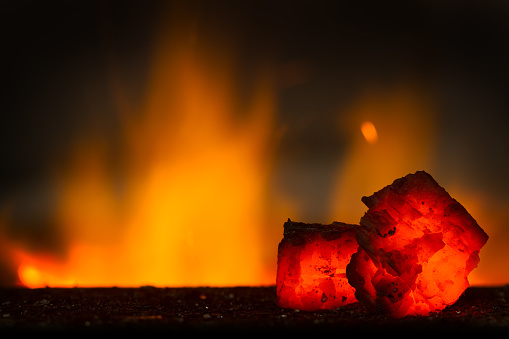 Red hot coal bars in focus on dark background with flames. Background of raw coal with soft focus exclusion with color and temperature.