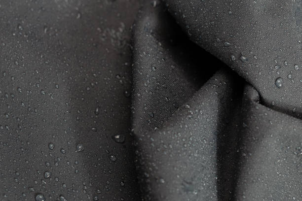 dark gray waterproof hydrophobic crumpled cloth closeup with rain drops selective focus background