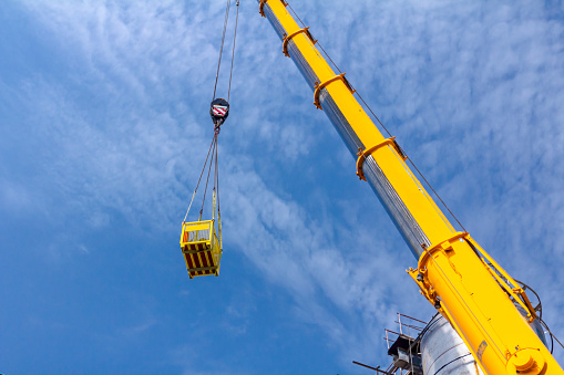 Crane hook with straps is raising work basket, palette high up to delivery equipment.