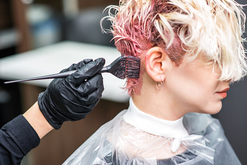 La mano del peluquero en guantes negros pinta el pelo de la mujer en un color rosa. photo